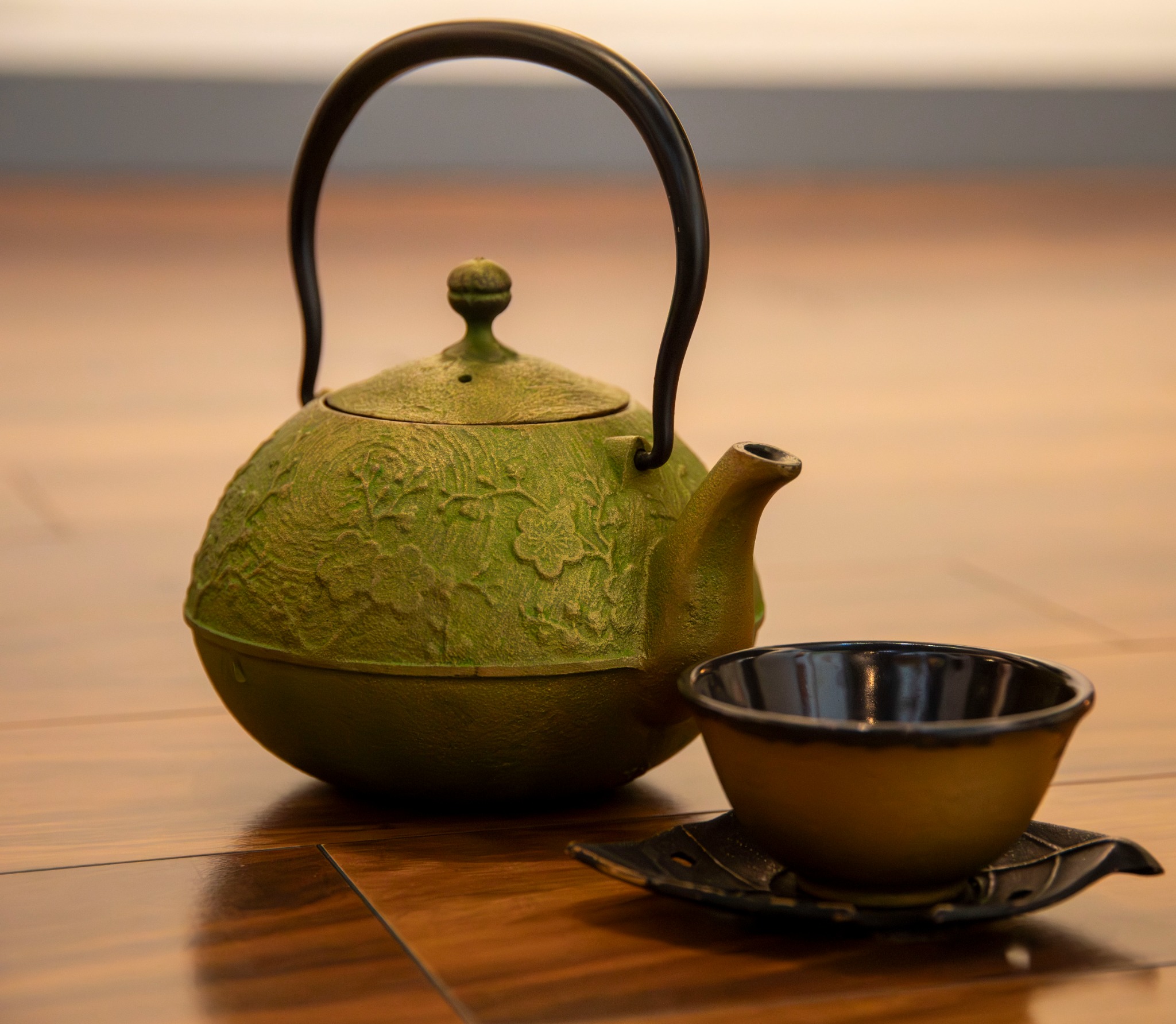A green cast-iron teapot with a small cup on a wooden floor